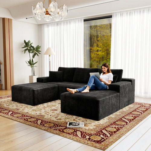 Woman sitting on a black sectional sofa in a living room with large windows.