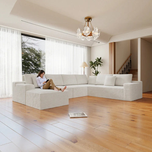 Woman sitting on a modern white sofa in a bright living room with large windows.
