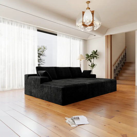 Modern living room with a black sectional sofa, wooden floor, and large windows.